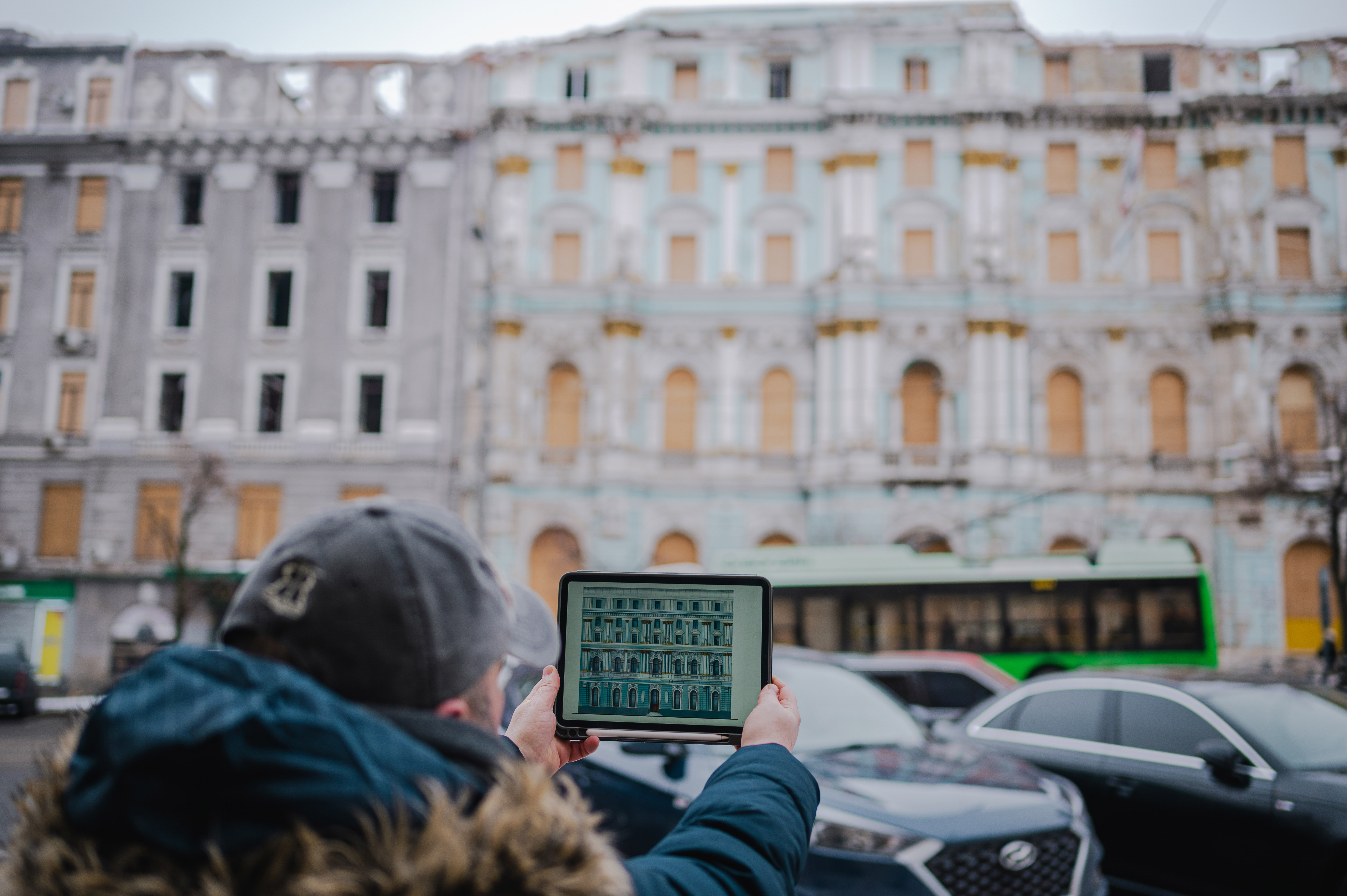 Maks, with a tablet in hand, aligns his restoration sketch with a historic building in central Kharkiv. ©Denis Vėjas