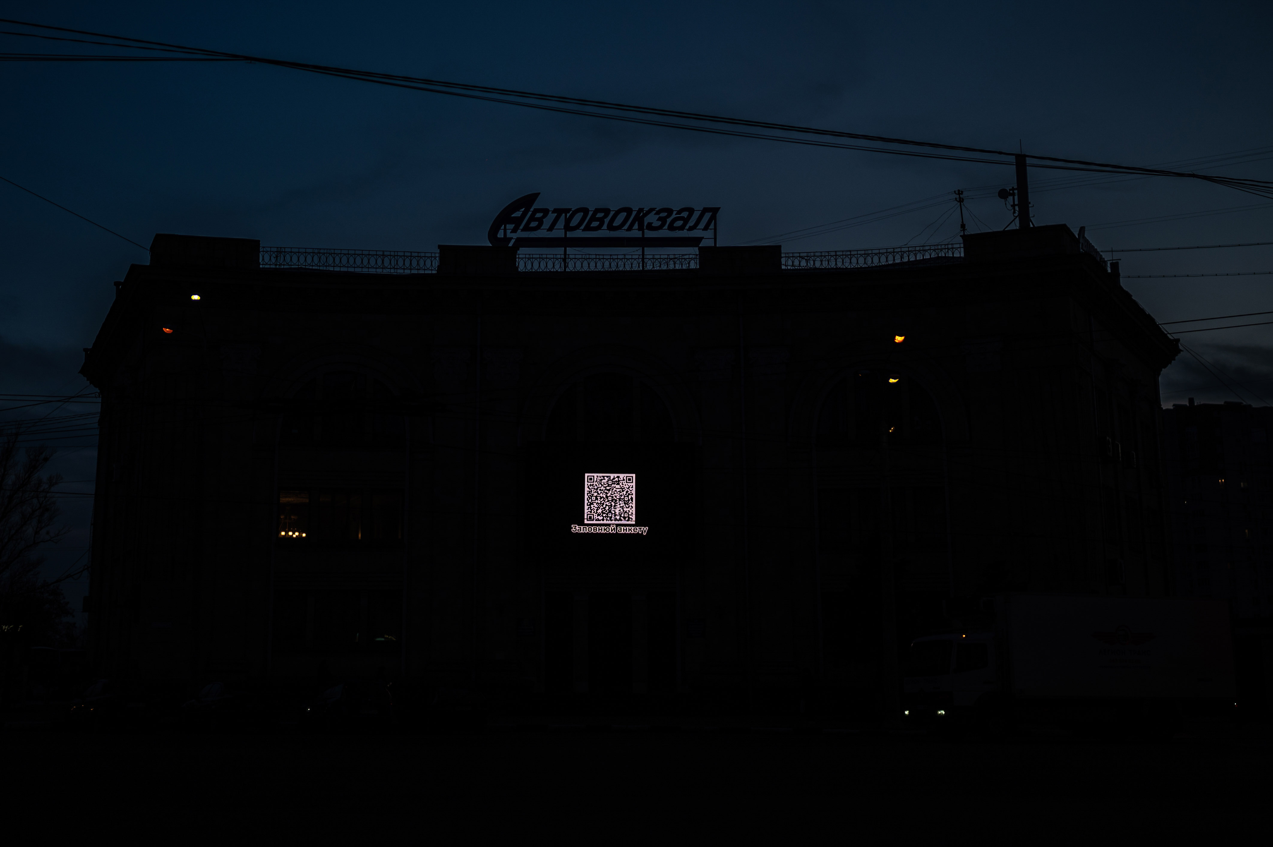 Nighttime in Kharkiv. A QR code glows on the side of the bus station building, linking to a military enlistment form. ©Denis Vėjas