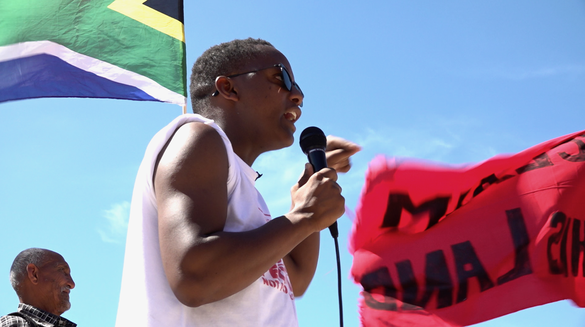 Nkosikhona Swartbooi speaking at one of the Reclaim the City protests in Cape Town. He becomes the narrator of Mother City documentary. Film still.