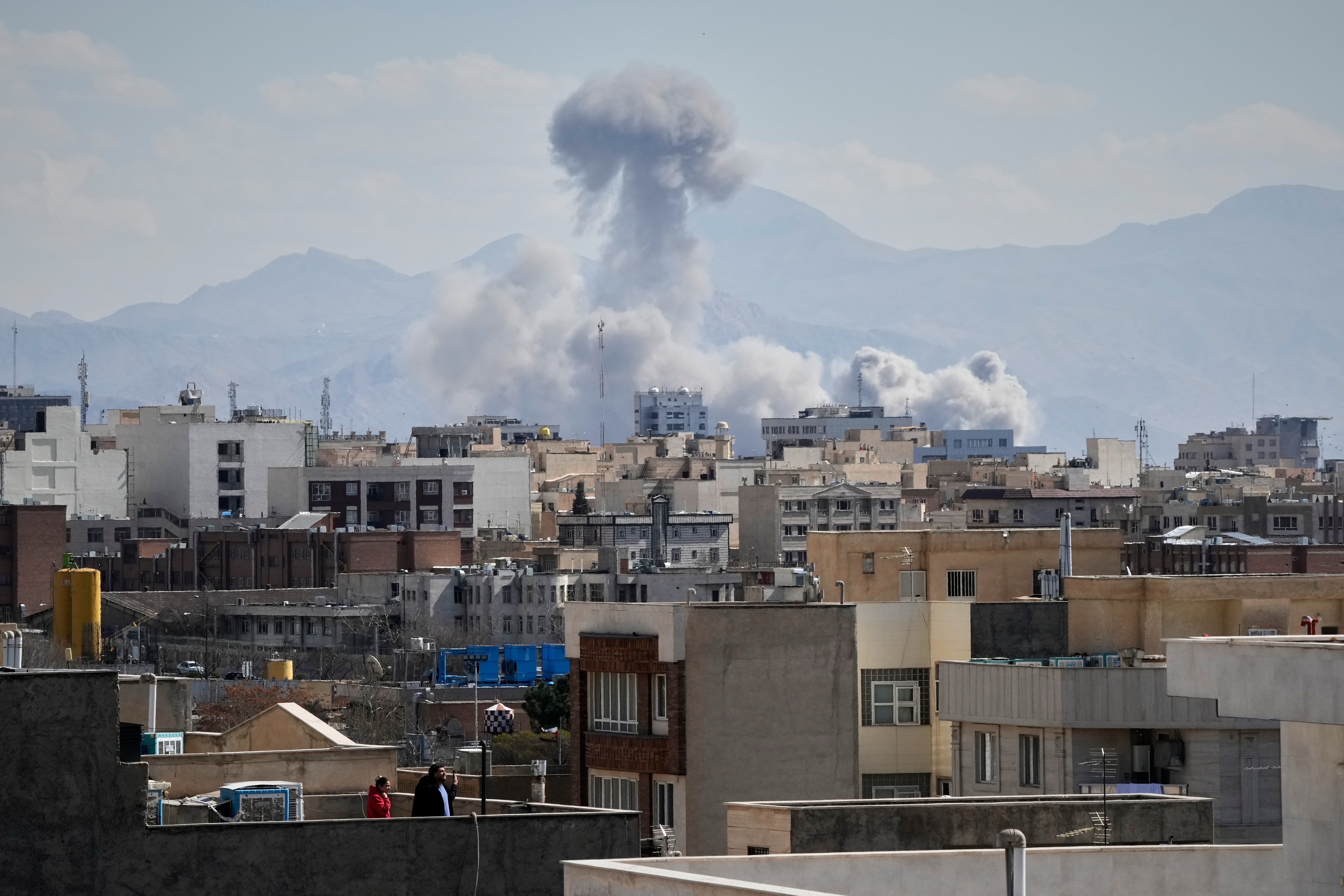 People watch from a rooftop as a plume of smoke rises after a strike in Tehran, Iran, Sunday, March 1, 2026. ©AP Photo/Vahid Salemi