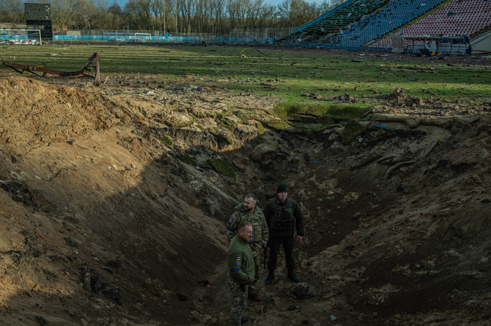 Ukrainiečių kariai tiria raketos paliktą kraterį Černihivo stadione.