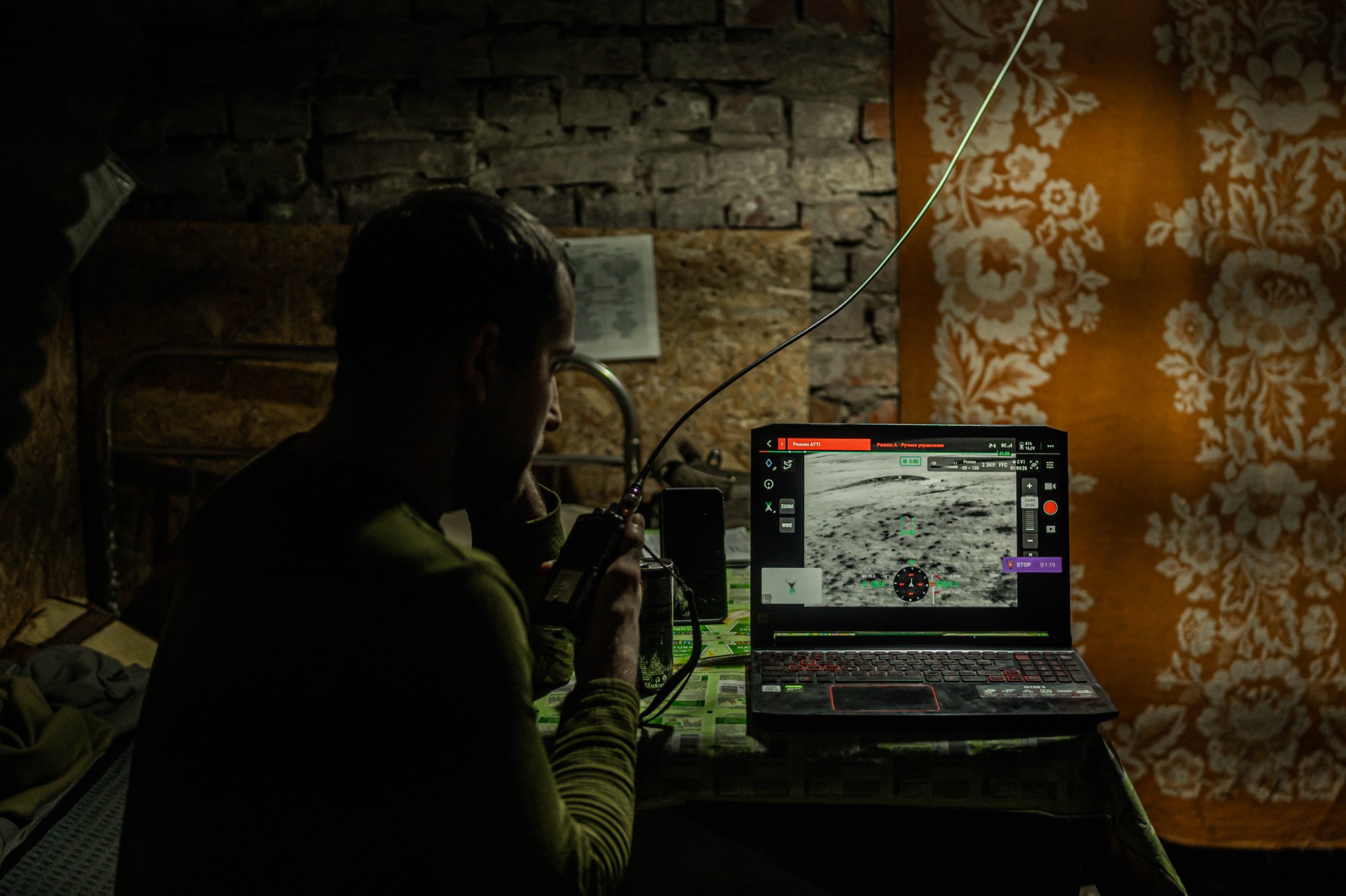 Ihoris įmeta malkų į krosnelę ir kompiuteryje rodo dronų filmuotą medžiagą, kurią analizuoja ieškodamas priešo pozicijų. Perjungus programos langelį galima stebėti dronų darbą realiu laiku. ©Denis Vėjas