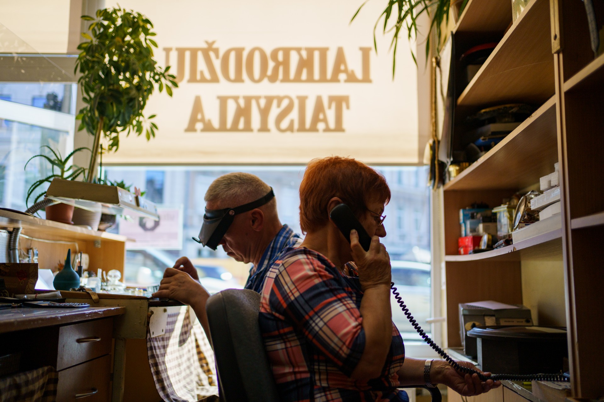 Kol Jonas taiso laikrodį, Irena skambina klientei pranešti, kad jos laikrodis jau sutaisytas ir galima ateiti jį pasiimti. ©Mindaugas Drigotas