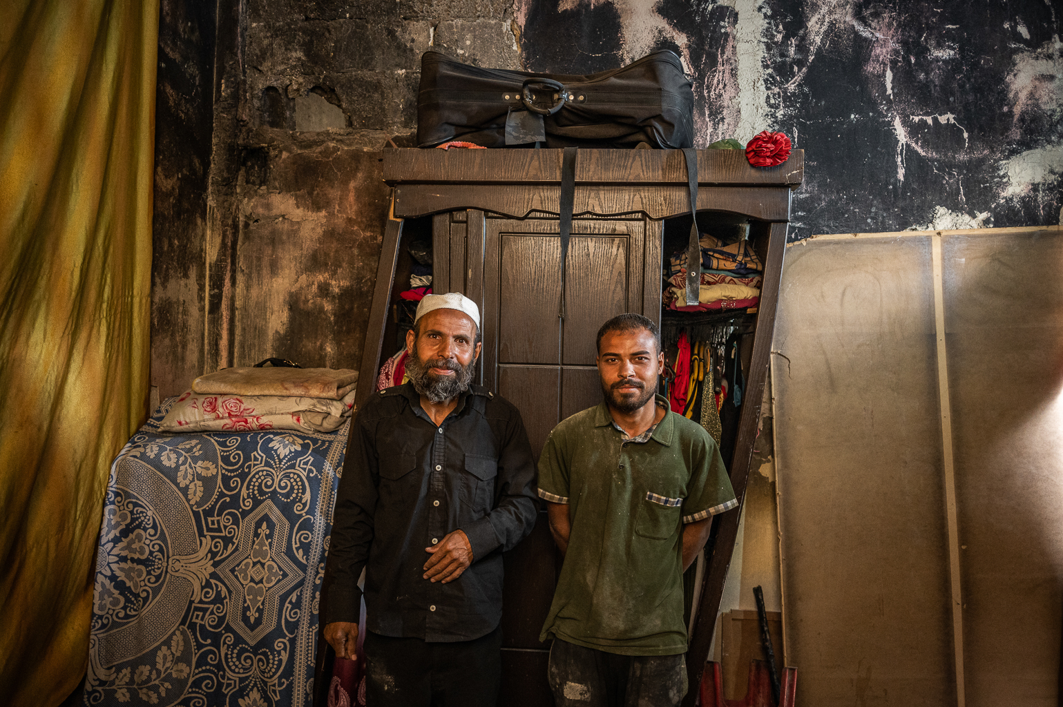 Teologas ir vietos šeichas Ahmadas Al-Masri su sūnumi savo namuose. Jų krosnelė – iš sugriuvusių namų plytų, o kambario sienos – juodų suodžių ornamentai. ©Denis Vėjas