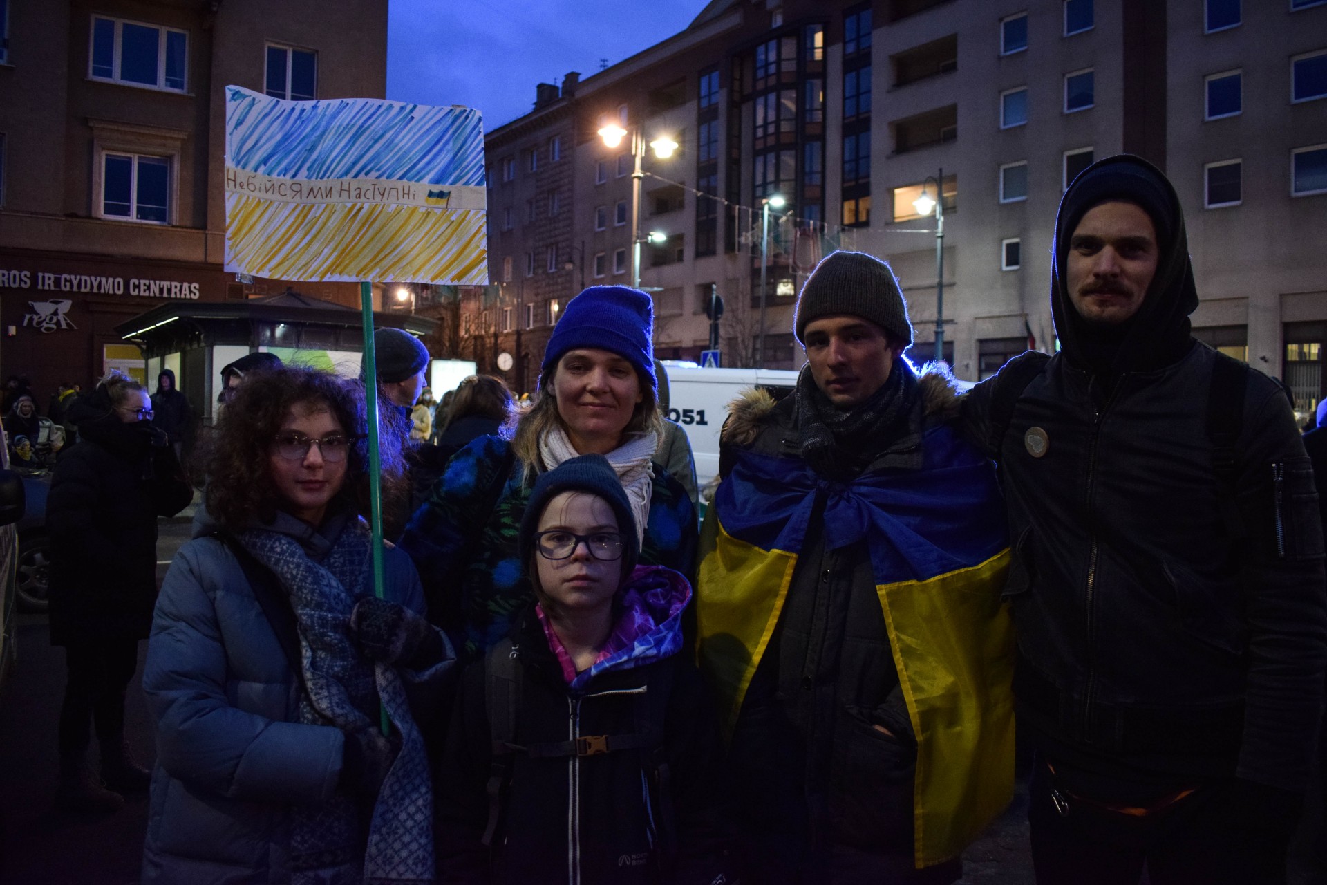 „Aš atsikėliau, kaip dažniausiai atsikeliu – su šypsena. Esu ukrainietis. Mano pirma kalba – ukrainiečių. Sužinojau iš savo draugų, šeimos, labai anksti ryte, kad „bombina“ visur, kad puola iš visų pusių, artilerija, lėktuvai. Aš, aišku, pradėjau skambinti. Buvau darbe ir nusprendžiau toliau dirbti, bet palaikiau kontaktą. Jaučiu labai daug nerimo ir streso, viduj toks... išsibalamutinę viskas. Bet aš žinau, kad tai nepadės ir, kad šiandien reikia stipriai laikytis. Ir kaip įmanoma padėti savo šeimoms. Aš, pavyzdžiui, labai norėčiau saugiai išvežti visus, bent jau mamą. Bet oro uostai uždaryti, siena uždaryta ir tiesiog blogiausias jausmas kokį tu gali turėti tai, kai tu žinai, kad tavo artimiausi žmonės, tie kuriuos labiausiai myli, jie nėra saugūs, jų gyvenimams gresia pavojus. Aš skambinu jiems ir vietoje to, kad pasakyčiau „Labas, kaip tu?“, sakau „Ar tave bombarduoja?“ arba „Susidėk kuprinę jeigu būtų evakuacija“. Tai nėra malonu, bet aš jaučiu labai stiprų palaikymą ir negaliu būti kitur nei čia. Lietuviai – mūsų broliai. Aišku, kad mūsų tiesa ir mes apginsim savo šalį. Bet tai bus už didelę kainą. Ir vien dėl to, kad kažkokiems žmonėms, idiotams, galvoj kažkoks marazmas. Reikia tik gintis ir kovoti už savo laisvę“, – sako Miša (nuotraukoje apsigaubęs vėliava). ©Julija Stankevičiūtė „Aš atsikėliau, kaip dažniausiai atsikeliu – su šypsena. Esu ukrainietis. Mano pirma kalba – ukrainiečių. Sužinojau iš savo draugų, šeimos, labai anksti ryte, kad „bombina“ visur, kad puola iš visų pusių, artilerija, lėktuvai. Aš, aišku, pradėjau skambinti. Buvau darbe ir nusprendžiau toliau dirbti, bet palaikiau kontaktą. Jaučiu labai daug nerimo ir streso, viduj toks... išsibalamutinę viskas. Bet aš žinau, kad tai nepadės ir, kad šiandien reikia stipriai laikytis. Ir kaip įmanoma padėti savo šeimoms. Aš, pavyzdžiui, labai norėčiau saugiai išvežti visus, bent jau mamą. Bet oro uostai uždaryti, siena uždaryta ir tiesiog blogiausias jausmas kokį tu gali turėti tai, kai tu žinai, kad tavo artimiausi žmonės, tie kuriuos labiausiai myli, jie nėra saugūs, jų gyvenimams gresia pavojus. Aš skambinu jiems ir vietoje to, kad pasakyčiau „Labas, kaip tu?“, sakau „Ar tave bombarduoja?“ arba „Susidėk kuprinę jeigu būtų evakuacija“. Tai nėra malonu, bet aš jaučiu labai stiprų palaikymą ir negaliu būti kitur nei čia. Lietuviai – mūsų broliai. Aišku, kad mūsų tiesa ir mes apginsim savo šalį. Bet tai bus už didelę kainą. Ir vien dėl to, kad kažkokiems žmonėms, idiotams, galvoj kažkoks marazmas. Reikia tik gintis ir kovoti už savo laisvę“, – sako Miša (nuotraukoje apsigaubęs vėliava). ©Julija Stankevičiūtė