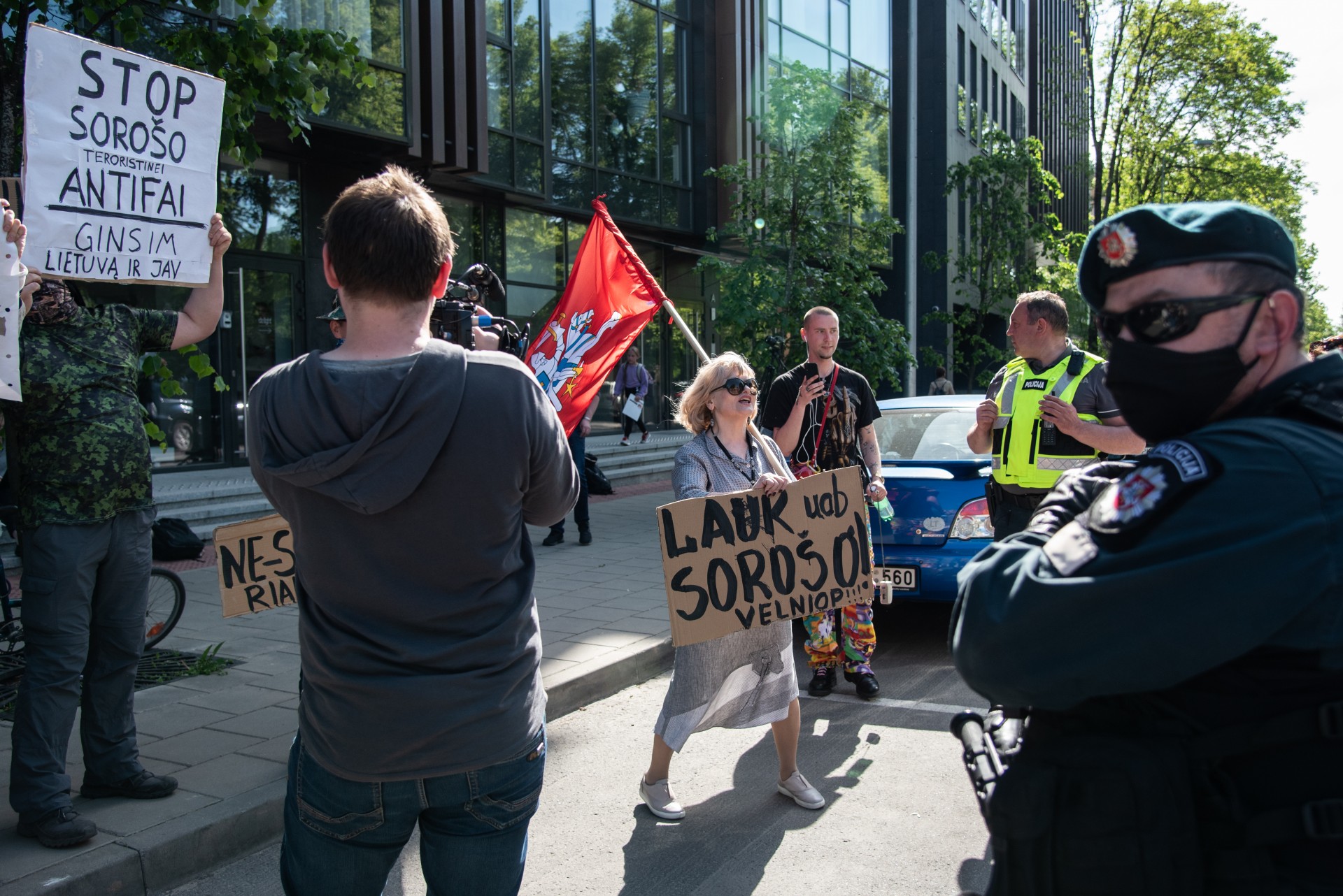Eitynių dalyvius prie JAV ambasados pasitiko maža grupė anti-protestuotojų. Vyčio vėliavą laikanti lietuvių kalbos mokytoja iš Vilniaus Juventos gimnazijos atsinešė plakatą, eitynių dalyvius siedama su žydu milijonieriumi George’u Sorosu. Per gegužės 30-ąją, kelios dienos po Floyd mirties, Tviteryje užfiksuota 500,000 žinučių su Soros’o vardu. Dauguma jų teigė, kad milijonierius moka protestuotojams JAV. Jungtinių Valstijų anti-šmeižto lyga tokį požiūriu laiko antisemitizmu. ©Severina Venckutė Eitynių dalyvius prie JAV ambasados pasitiko maža grupė anti-protestuotojų. Vyčio vėliavą laikanti lietuvių kalbos mokytoja iš Vilniaus Juventos gimnazijos atsinešė plakatą, eitynių dalyvius siedama su žydu milijonieriumi George’u Sorosu. Per gegužės 30-ąją, kelios dienos po Floyd mirties, Tviteryje užfiksuota 500,000 žinučių su Soros’o vardu. Dauguma jų teigė, kad milijonierius moka protestuotojams JAV. Jungtinių Valstijų anti-šmeižto lyga tokį požiūriu laiko antisemitizmu. ©Severina Venckutė