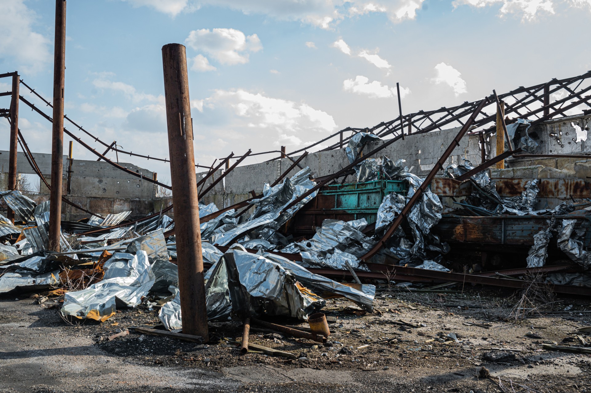 Valerijaus ūkio griuvėsiai. Sandėliavimo angarų metaliniai karkasai susiraitę nuo karščio, aplink – sudeginta ir surūdijusi darbo technika. ©Denis Vėjas